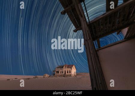 A beautiful night sky photograph with circular star trails against a deep blue sky, with an abandoned house and desert sand in the background, taken i Stock Photo