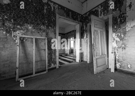 A black and white photograph inside an abandoned house with an open doorway, taken in the ghost town of Kolmanskop, Namibia. Stock Photo
