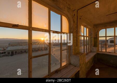 A dramatic photograph inside an abandoned house at sunrise, with a golden  sunburst and building through broken windows, taken in the ghost town of Ko Stock Photo