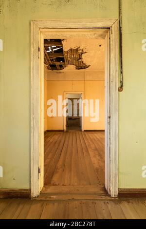 A vertical photograph inside an abandoned house with an open doorway leading into another room, taken in the ghost town of Kolmanskop, Namibia. Stock Photo