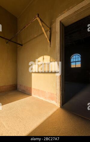 A vertical photograph inside an abandoned house with an open doorway leading into another room and a shaft of golden light streaming in the room, take Stock Photo