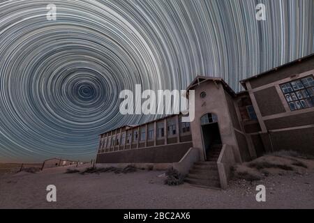 A spooky and dramatic night sky photograph of the old hospital building with circular star trails and desert sand, taken in the ghost town of Kolmansk Stock Photo