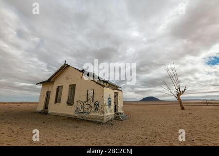 A spooky  desert landscape taken near Luderitz, Namibia, with an abandoned old house covered in grafitti and a dead tree against a dark, stormy and mo Stock Photo