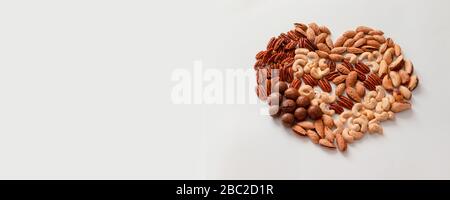 Creative composition of assorted walnut pecans, macadamis, brazil nut, cashews, almonds on gray background. Mix nuts heart shape. Diet, proper balancing nutrition concept Stock Photo