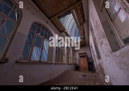 A dramatic night sky taken inside an abandoned building with star trails appearing through the broken roof and desert sand and a door inside the room, Stock Photo
