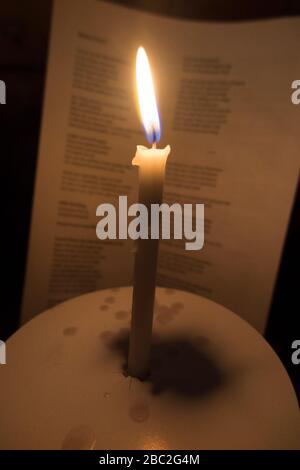Church candle with a burning flame photographed during a Christmas carol service concert at Xmas. The words of the carols are visible on the hymn sheet behind. England UK (116) Stock Photo