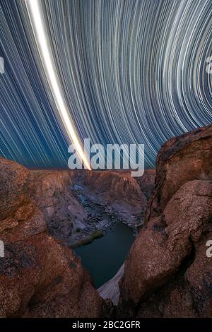 A majestic vertical night sky star trail photograph with the Moon streaking through the sky, with views of the river and mountains at the Augrabies Fa Stock Photo