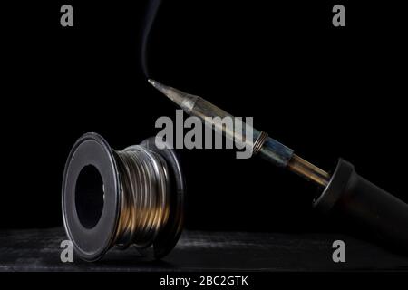 Smoky soldering iron and solder wire bobbin on a black background Stock Photo