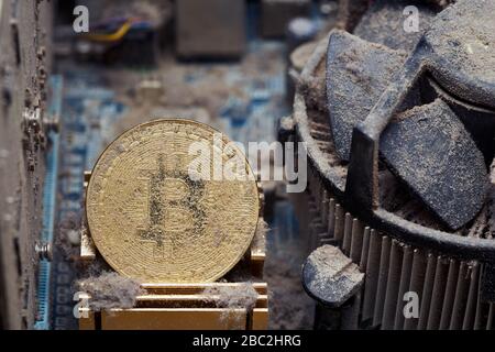 Dirty golden bitcoin inside an old broken computer covered with dust Stock Photo