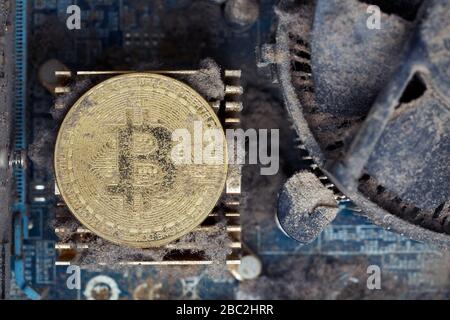 Dirty golden bitcoin inside an old broken computer covered with dust Stock Photo