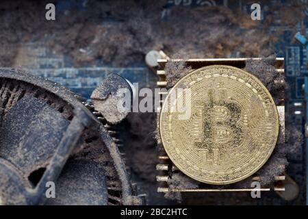 Dirty golden bitcoin inside an old broken computer covered with dust Stock Photo