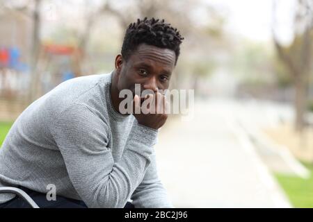 Portrait of a serious black man looking at camera sitting in the park bench Stock Photo