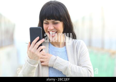 Happy adult woman laughing checking smart phone content on a bridge Stock Photo