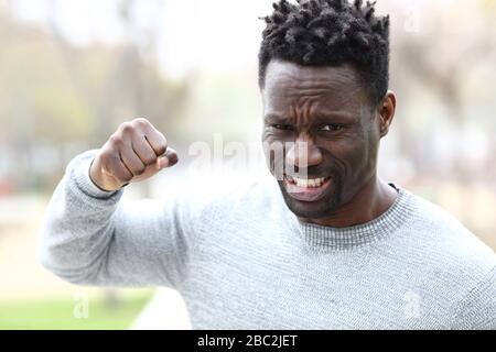 Front view portrait of an angry black man threatening with fist looking at camera in the park Stock Photo