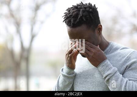 Black allergic man scratching itchy eyes standing in a park in winter Stock Photo