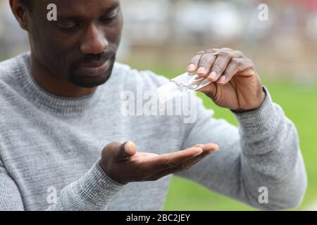 Black man cleaning hands with sanitizer soap outdoors in a park Stock Photo
