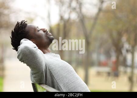 Side view portrait of a black man relaxing sitting on a bench in a park Stock Photo