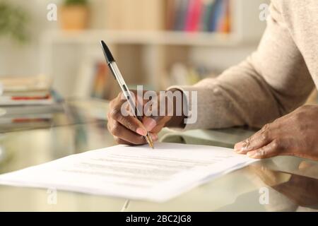 Close up of black man hands signing document on a desk at home Stock Photo
