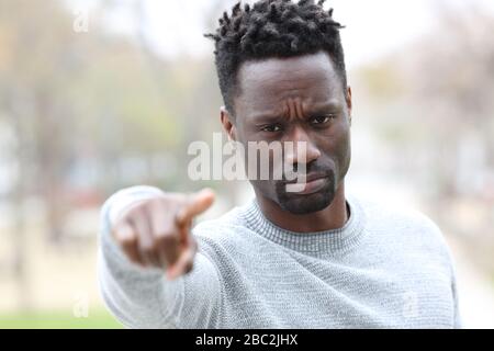 Front view portrait of a black serious man looking at camera pointing at you in a park Stock Photo