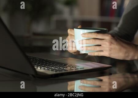 Close up of girl hands watching media on laptop at night with a coffee cup on a desk at home Stock Photo