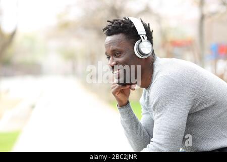 Happy black man listening to music with headphones sitting in the park Stock Photo
