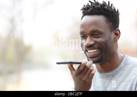Happy black man using voice recognition on smart phone outdoors in a park Stock Photo