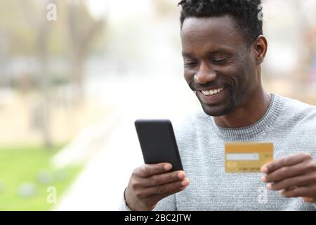 Happy black man paying online with credit card on smart phone in the park Stock Photo