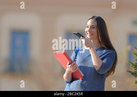 Happy student using voice recognition on cell phone standing outdoors in a university campus Stock Photo