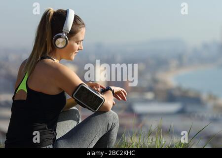 Runner wearing headphones checks music on smartwatch outdoors in city outskirts Stock Photo