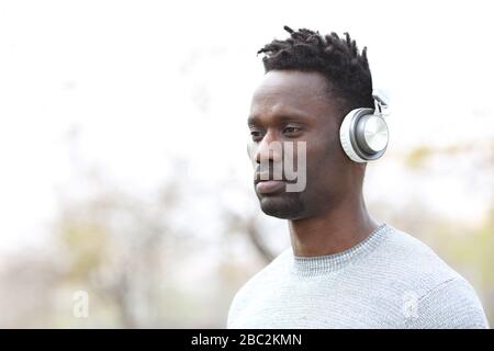 Serious black man listening to music wearing wireless headphones outdoors Stock Photo