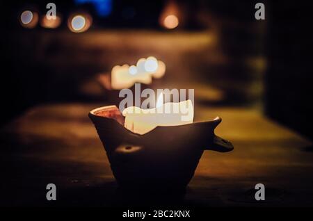 antique clay candlestick with a burning candle stands on a wooden table in a dark room Stock Photo
