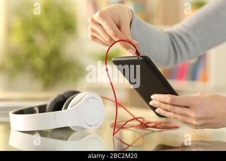 Close up of woman hands plugging headphones to smart phone on a desk at home Stock Photo