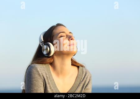 Relaxed woman wearing headphones meditating listening to music on the beach at sunset