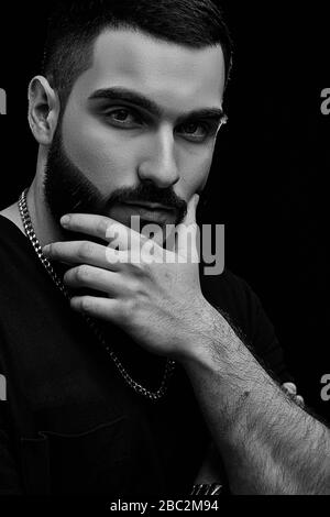 a dramatic portrait of a young serious guy, musician, singer, rapper with a beard in black clothes on a black isolated background. he is thinking care Stock Photo