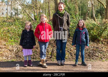 Mother & 3 children three kids daughters pose proudly with trees in woodland whilst walking / on walk path / walkway pathway foot path footpath. West End Common near Esher in Surrey, England UK (116) Stock Photo