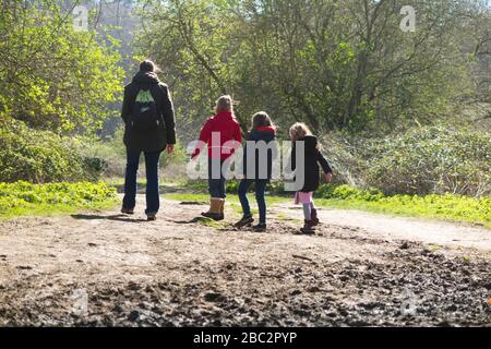 Mother & 3 children three kids daughters walking / walk along muddy path / in mud on walkway pathway foot path footpath. West End Common, near Esher, Surrey. UK (116) Stock Photo
