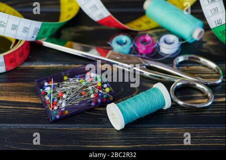 macro color photo of different sewing tools like scissors and sewing thread on wooden table Stock Photo