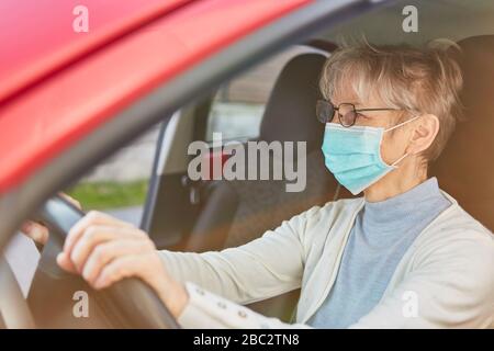 Elderly woman wearing a face mask driving a car because of the Covid-19 coronavirus pandemic Stock Photo