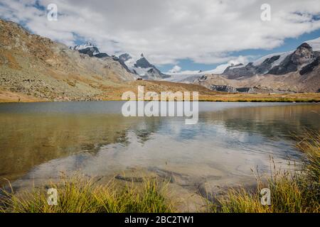 Small red tourists shelter house and beautiful mountains lake with snowy peaks of Swiss Alps reflection Stock Photo