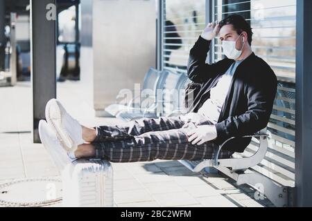 A man is waiting for a train on the platform, wearing a face mask and rubber gloves to protect himself from the corona virus Stock Photo