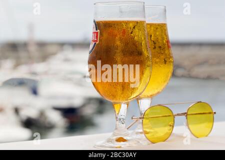 Two misted glasses of cold beer and sunglasses on the background of the marina and yachts in the port. Stock Photo