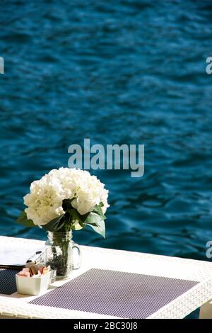 Beautiful place for dinner by the sea with white flowers. Shoreside table setting ready for new customers. Lot of copy-space Stock Photo