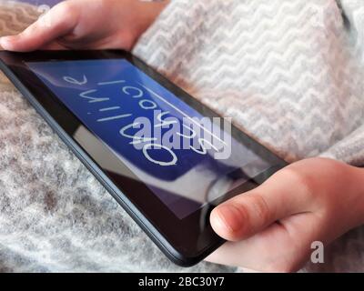 A tablet in the hands of a child with the text online school on the background of a gray plaid.The concept of distance learning,online learning at Stock Photo
