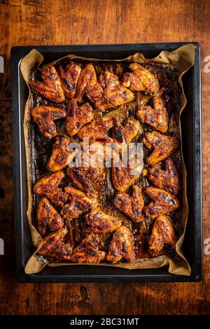 Grilled chicken wings in barbecue sauce in baking tray on wooden table. Top view.