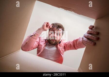 Man looks in bewilderment at the newly unpacked box with the parcel. Delivery error or defective item. Unboxing inside view. Stock Photo