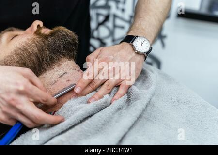 Shaving process of beards in Barbershop. Close up shot of barber makes a haircut beard client with straight razor. Stock Photo
