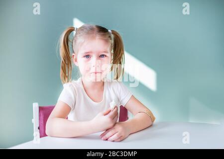 Little blonde girl with two ponytales is crying sitting by the white ...