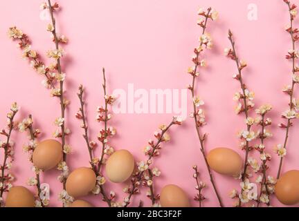 Easter holiday background. Flat-lay of tender Spring  blossom flowers on branches, feathers, eggs over light pink background, top view, copy space, wi Stock Photo