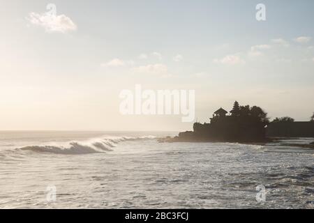 Backlit outline of Pura Tanah Lot Balinese sea temple with crashing waves on the pebble beach, Denpasar, Bali, Indonesia Stock Photo