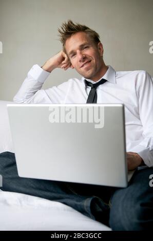 Man in jeans and skinny black tie sitting on the sofa browsing his laptop computer Stock Photo